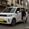 BYD Racco electric kei car in white with a man entering through sliding door on a narrow street in Japan