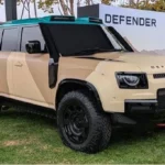 Land Rover Defender Dakar SUV driving through desert dunes, AutoAkhbar branded image
