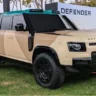 Land Rover Defender Dakar SUV driving through desert dunes, AutoAkhbar branded image