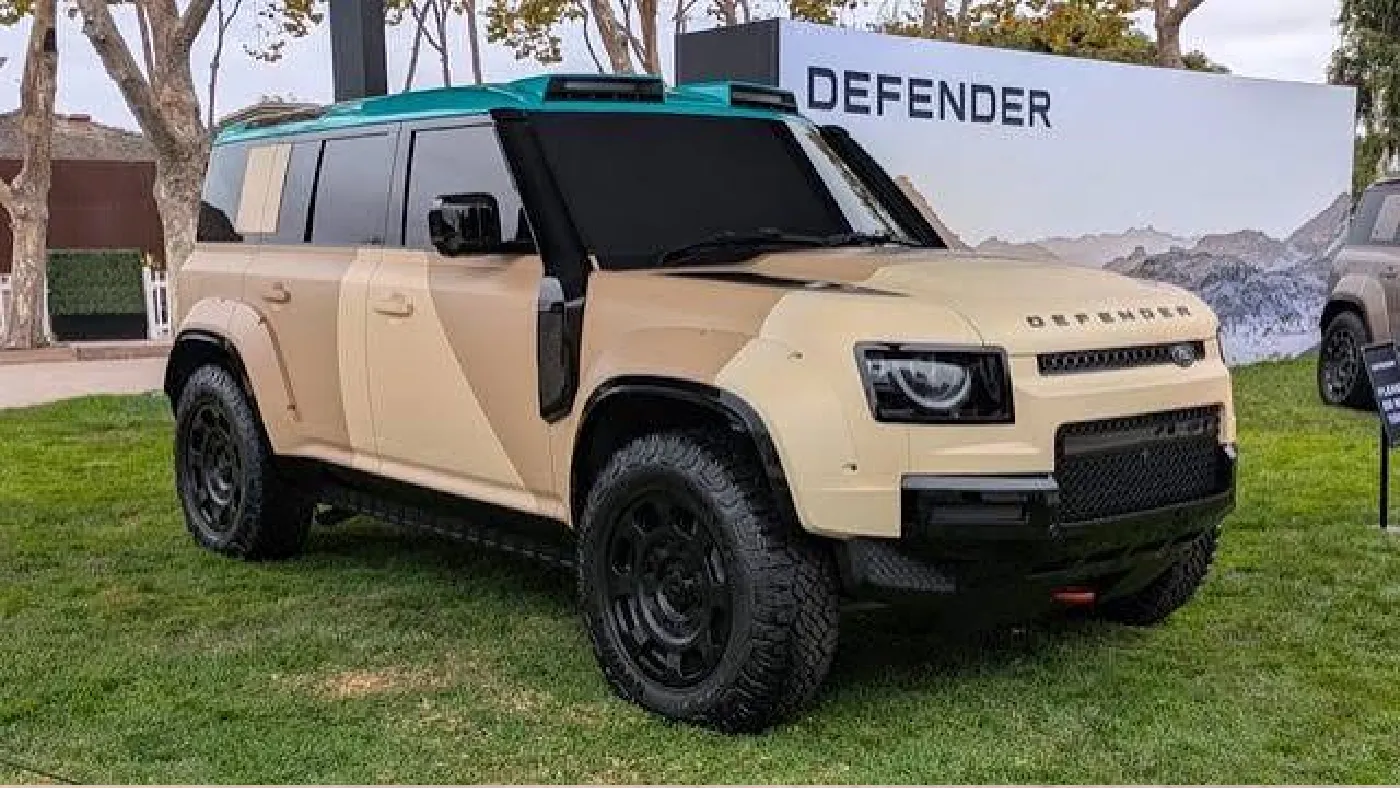 Land Rover Defender Dakar SUV driving through desert dunes, AutoAkhbar branded image