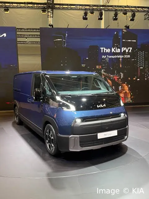 Blue Kia PV7 Cargo electric van displayed at the IAA Transportation 2026 exhibition with a city skyline backdrop screen.