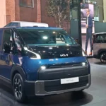 Deep blue Kia PV7 Cargo electric van displayed on a rotating stage at a Kia PBV motor show event with a presenter standing in the background.