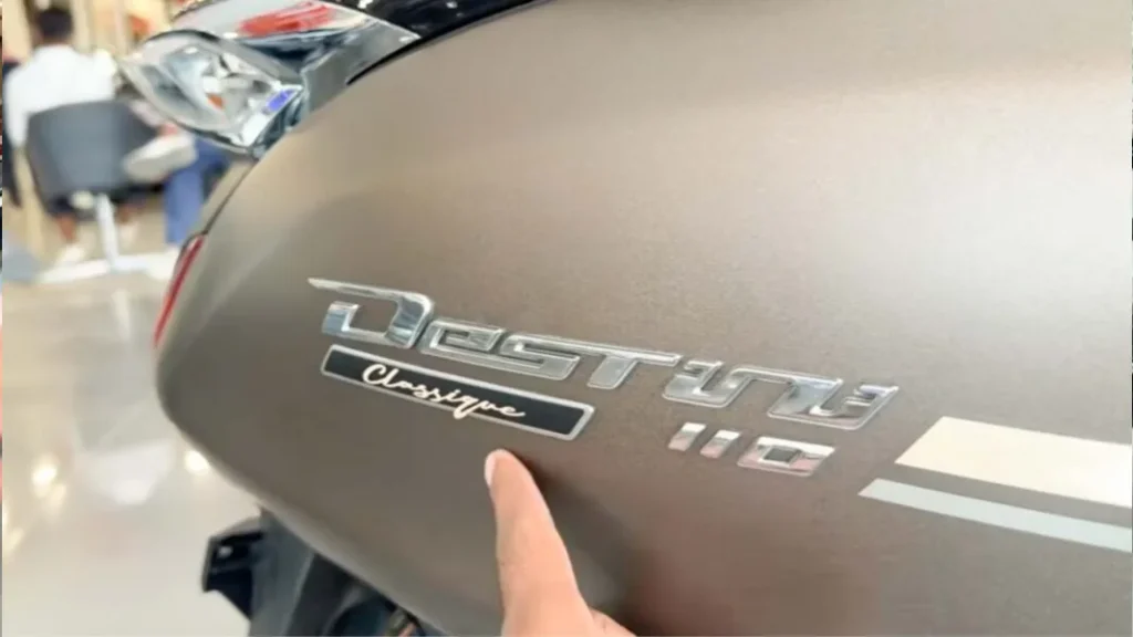 Close-up shot of the premium chrome 3D Destini 110 badge featuring a dedicated script Classique emblem on the side panel of the scooter.