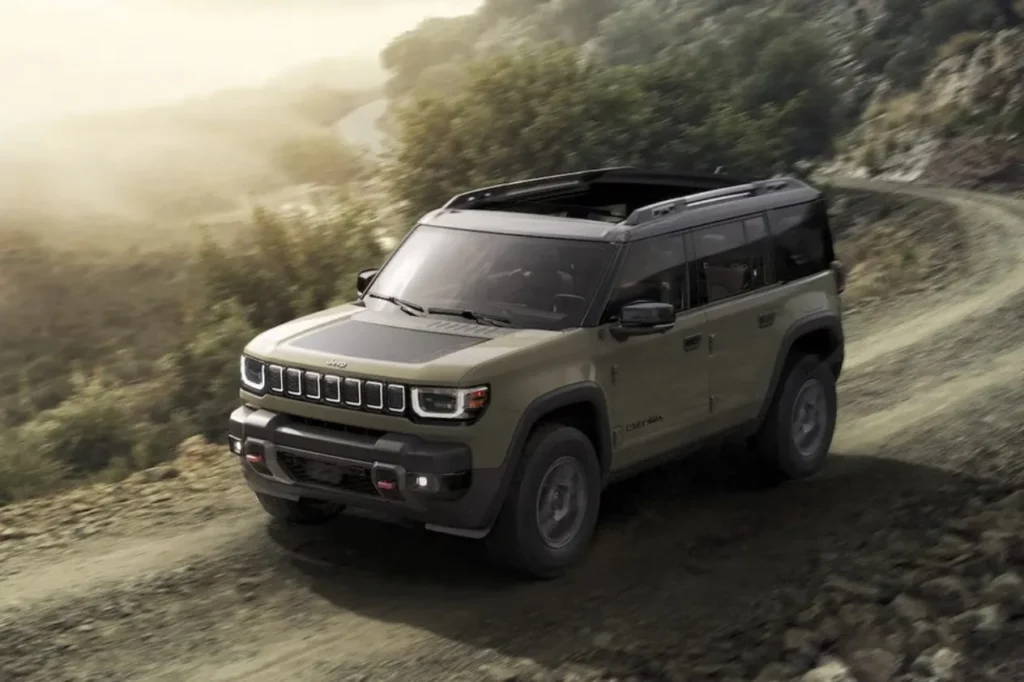 Electric Jeep : An olive green Jeep Recon all-electric SUV driving on a rugged dirt mountain trail, showcasing its off-road capability during a range test.