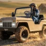A side-angle dynamic shot of a person wearing a helmet driving a cream-colored Massimo mini truck go-kart while kicking up a trail of dust on a rocky desert path during golden hour.
