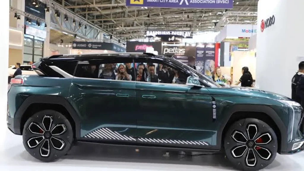 A side-angle profile shot of the dark metallic green Nobo iNest 3.0 electric concept SUV showcased at the IAA Mobility expo, highlighting its futuristic alloy wheels, geometric body contours, and flat rear roofline.