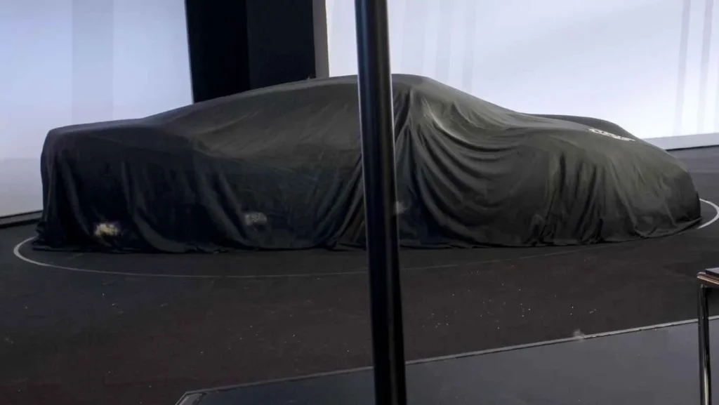 A mysterious dark studio display featuring the highly anticipated Porsche Mission S concept hypercar completely concealed under a tight premium black silk cover sheet, emphasizing its aggressive low-slung track proportions and aerodynamic lines with soft ambient floor smoke.