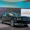 A front view of a majestic glossy black Toyota Century ultra-luxury flagship limousine parked against a dramatic cloudy sunset sky, showcasing its executive wheelbase, signature multi-spoke chrome wheels, and phoenix emblems on the center caps.