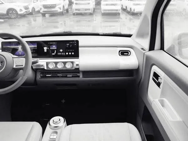 A close-up interior view of the modern white and gray Wuling Air EV dashboard, showcasing the twin integrated digital infotainment display screens, a minimalist two-spoke steering wheel, and sleek climate control dials.